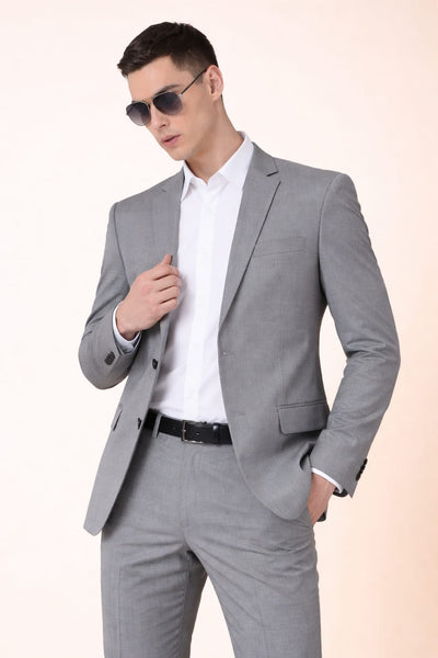 Man wearing a gray suit with sunglasses on a light pink background