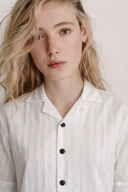 Person wearing a light-colored shirt with black buttons against a plain background