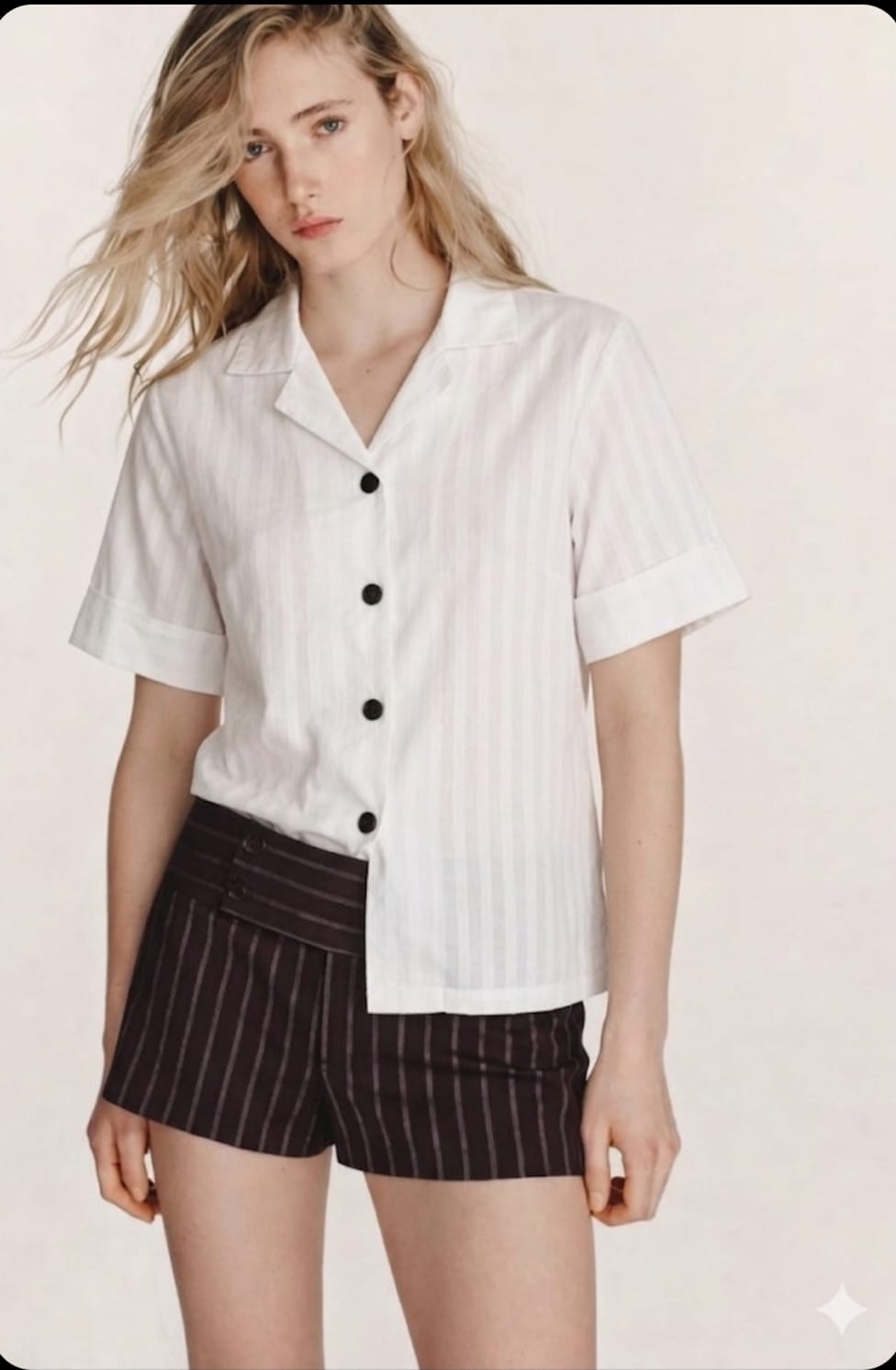 Woman wearing a white button-up shirt and black pinstripe shorts on a plain background