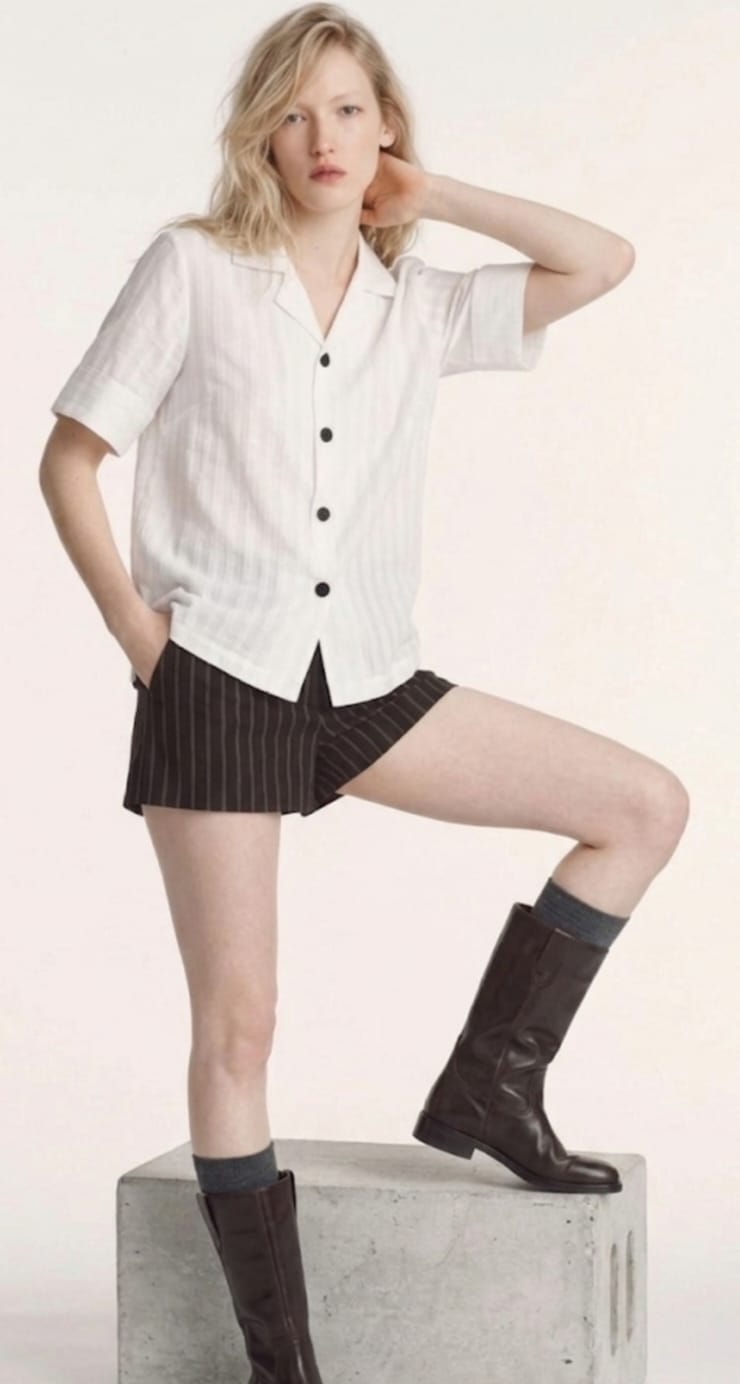 Woman wearing a white shirt, black skirt, and brown boots on a light background