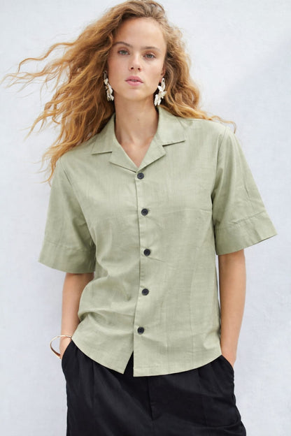 Woman wearing a light green button-up shirt with black pants against a white background