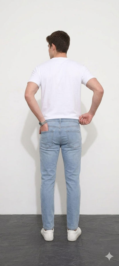 Person wearing a white t-shirt and light blue jeans standing against a white wall.