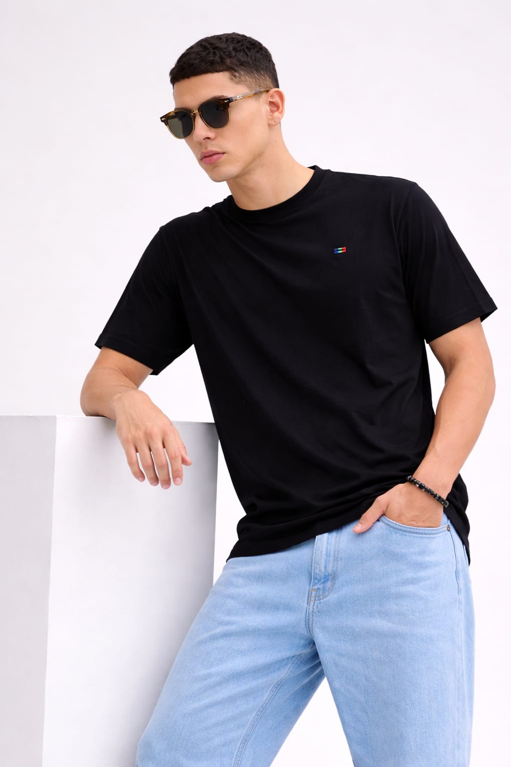 Man wearing a black t-shirt and light blue jeans against a white background