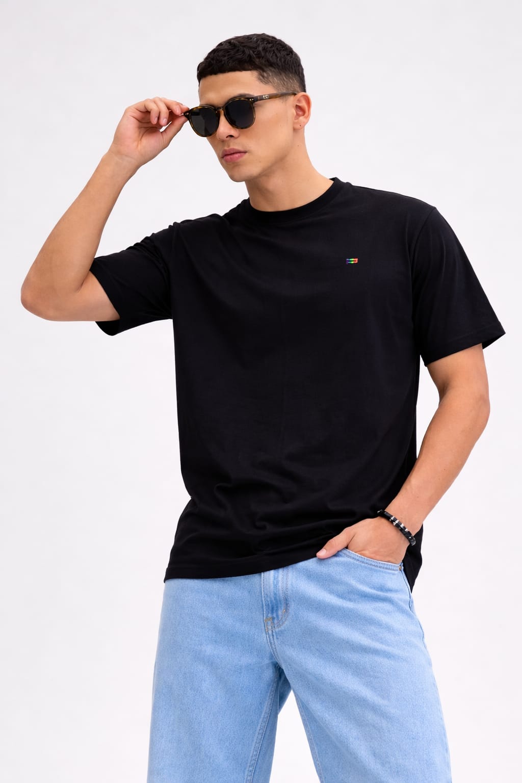 Man wearing a black t-shirt and light blue jeans with sunglasses on a white background