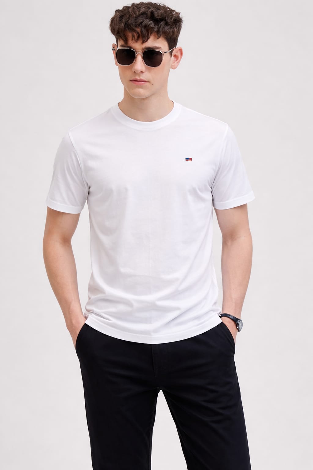 Man wearing a white t-shirt with a logo and black pants on a light gray background