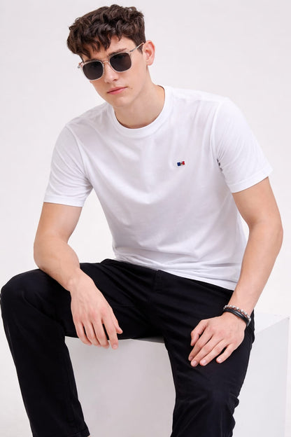 Man wearing a white t-shirt with a small logo and black pants, sitting on a white background.