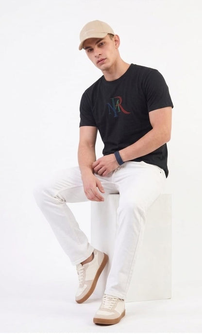 Man wearing a black t-shirt with a logo, white pants, and a beige cap on a white background