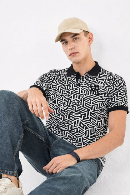 Man wearing a black and white geometric patterned polo shirt with a beige cap and jeans, sitting on a white background.