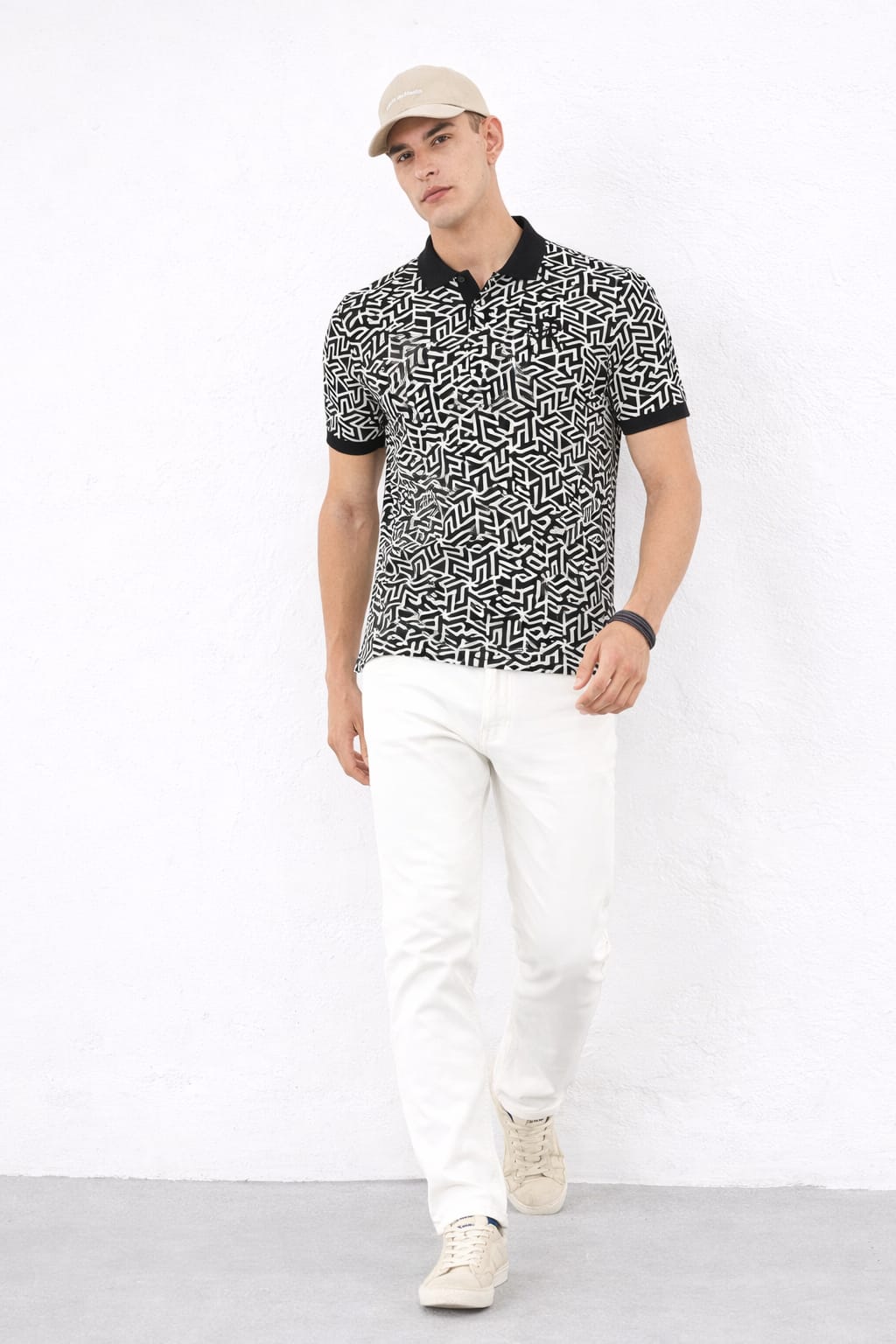 Man wearing a patterned black and white shirt with white pants on a white background