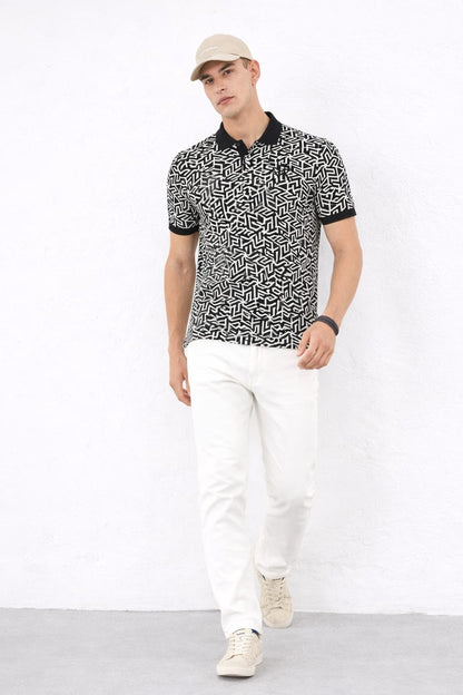 Man wearing a patterned black and white shirt with white pants on a white background