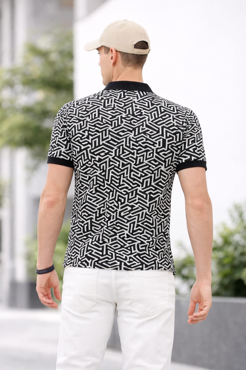 Man wearing a black and white patterned polo shirt with a cap, standing outdoors.