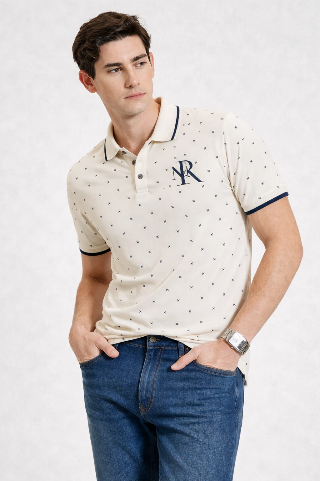 Man wearing a patterned polo shirt with a logo and blue jeans on a white background