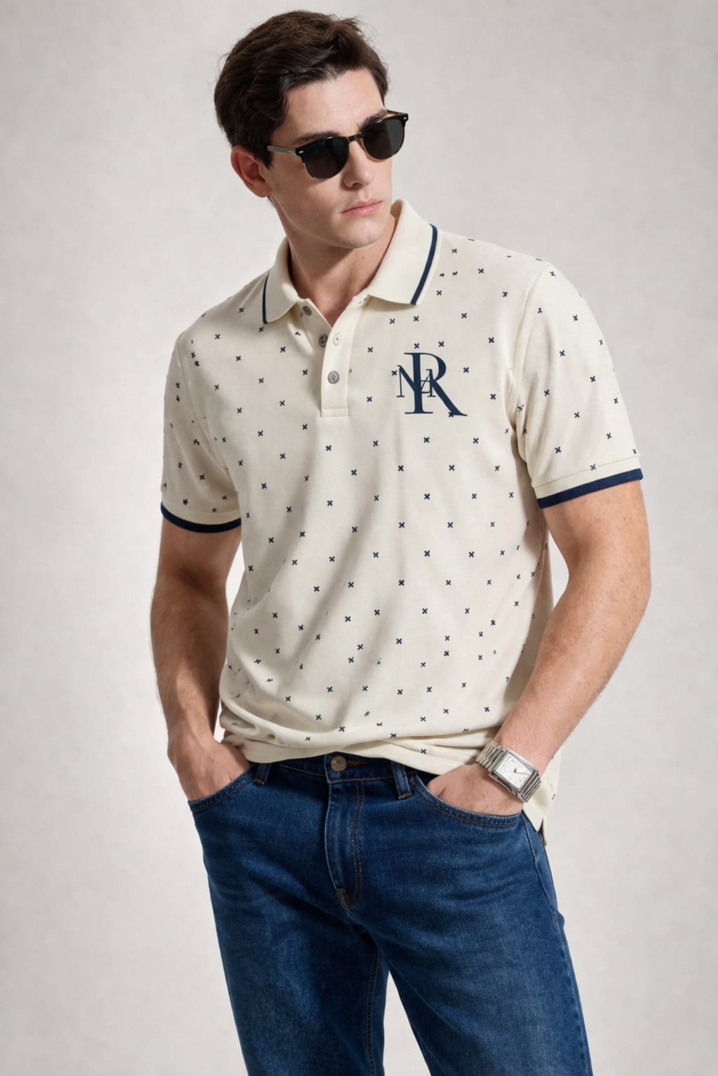 Man wearing a patterned polo shirt with a logo and sunglasses on a plain background