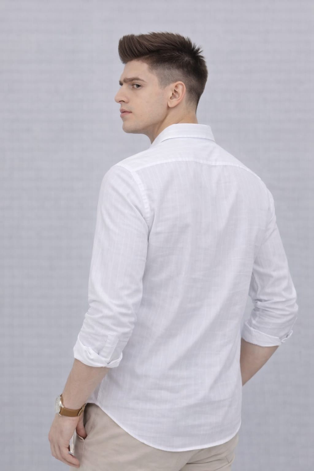 Man wearing a patterned polo shirt with a logo, sitting on a wooden stool against a plain background