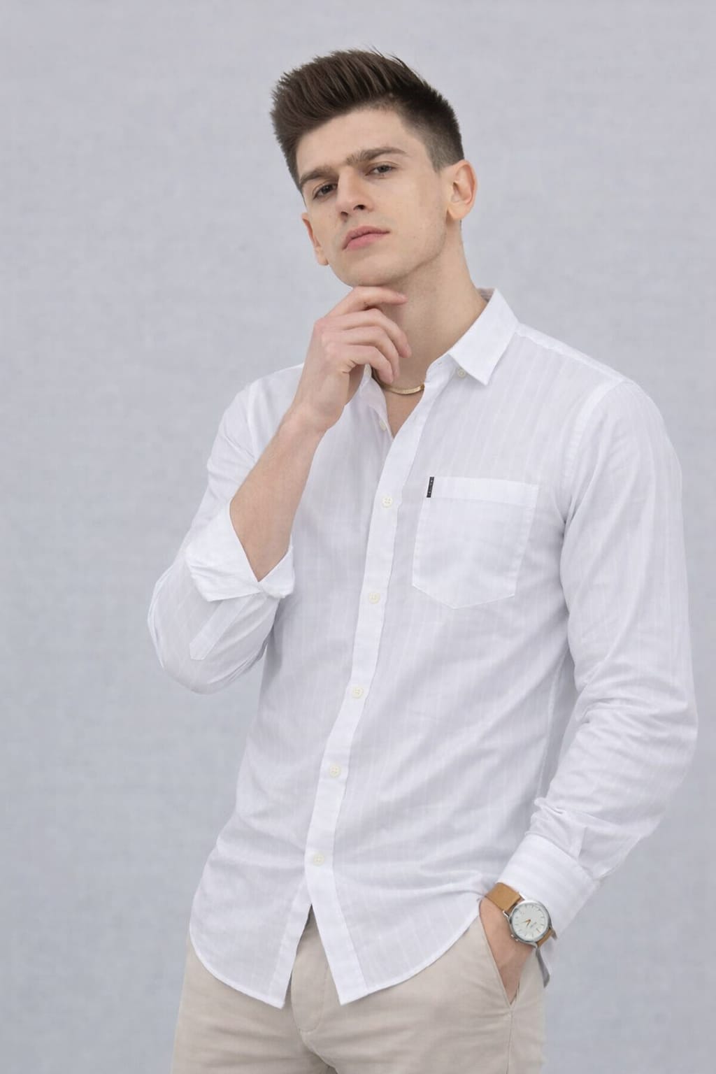 Man wearing a patterned polo shirt with a logo, sitting on a wooden stool against a plain background