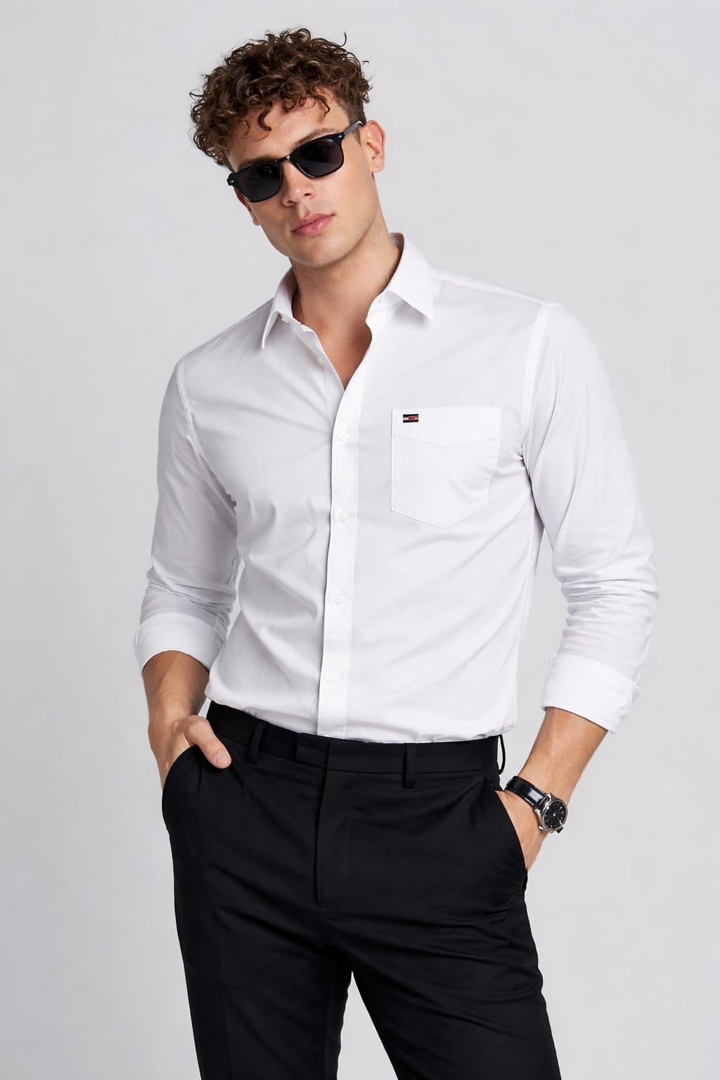Man wearing a white dress shirt and black pants with sunglasses on a light gray background