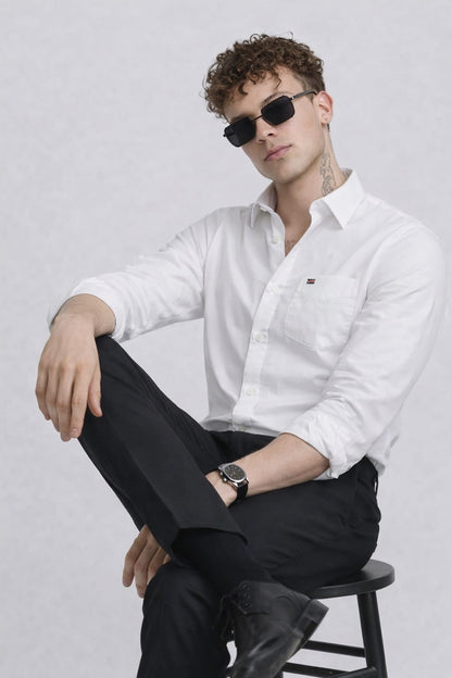Man wearing a white shirt and black pants sitting on a stool against a plain background