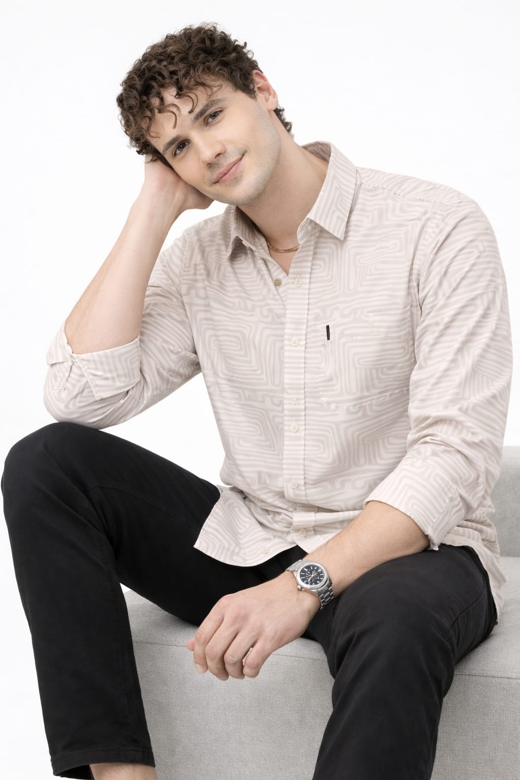 Man sitting on a white couch wearing a light-colored shirt and black pants, with a neutral background.