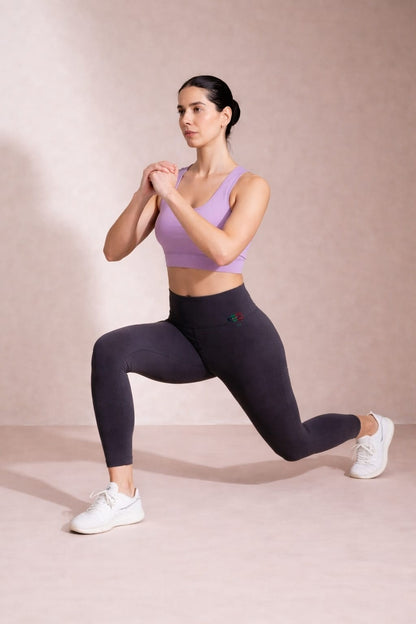Woman in athletic wear performing a lunge on a plain background