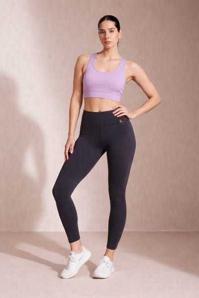 Woman wearing a purple sports bra and black leggings on a beige background