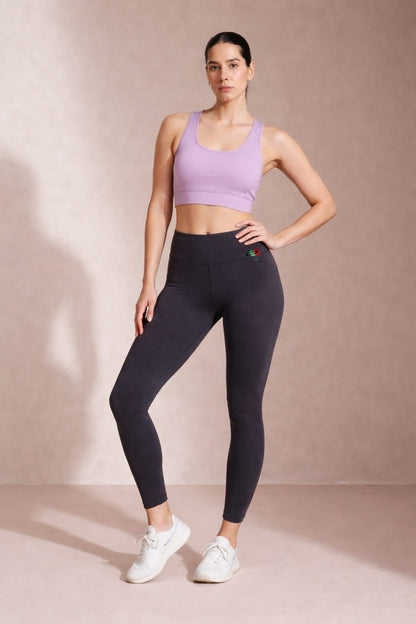 Woman wearing a purple sports bra and black leggings on a beige background