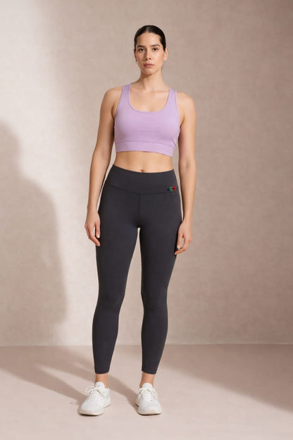 Woman wearing a purple sports bra and black leggings against a beige background