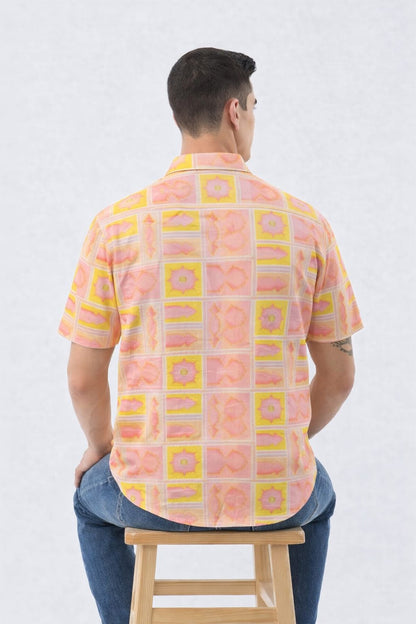 Man wearing a patterned shirt sitting on a stool against a white background