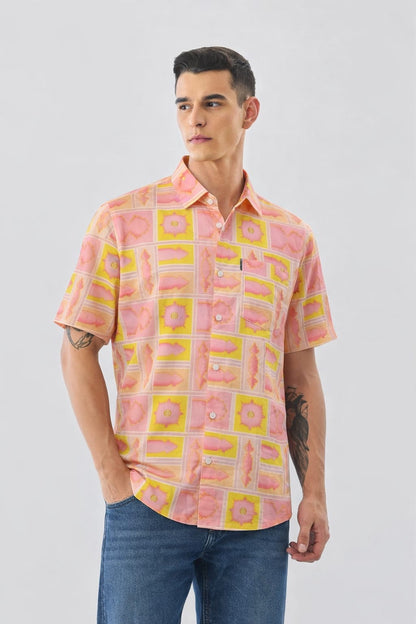 Man wearing a patterned pink and yellow shirt with blue jeans on a white background
