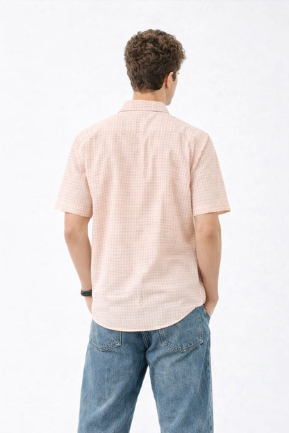 Man wearing a light pink checkered shirt and blue jeans on a white background