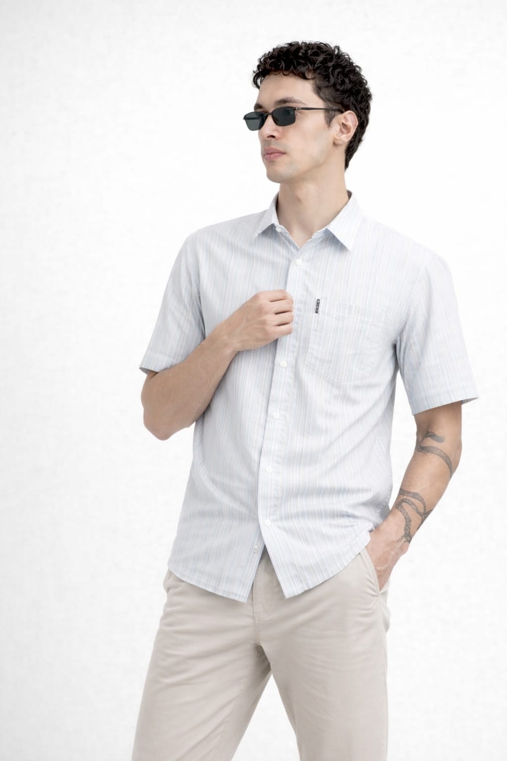 Man wearing a light gray short-sleeve shirt and beige pants on a white background
