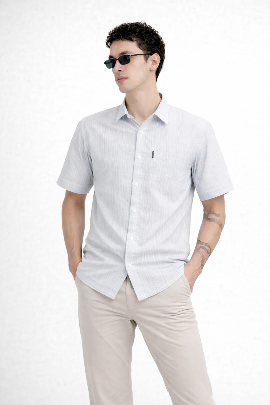 Man wearing a light gray short-sleeve shirt and beige pants on a white background