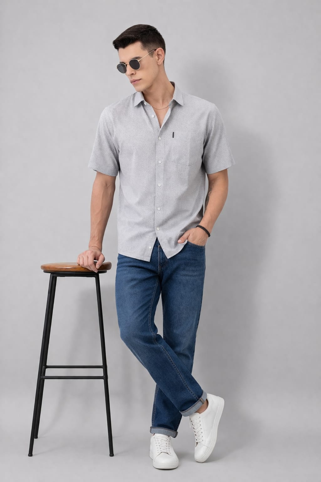 Man wearing a light gray button-up shirt, blue jeans, and white sneakers on a gray background