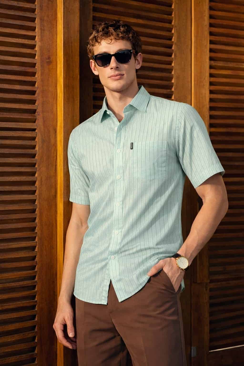 Man wearing a light blue striped shirt and sunglasses against a wooden background
