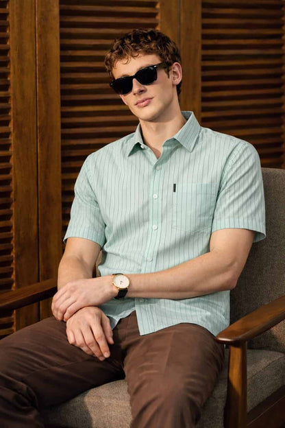Man wearing a light green striped shirt and sunglasses against a wooden background